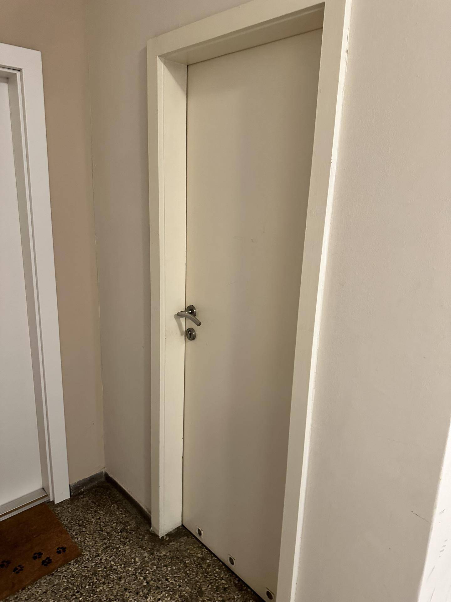 Eine schlichte weiße Tür in einem Flur mit hellem Terrazzoboden, typisch für ein Mehrfamilienhaus.