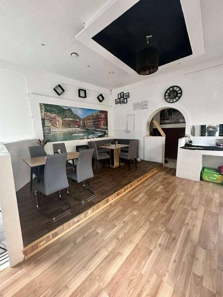 Innenbereich eines Restaurants mit erhöhter Sitzecke, Holzboden und Wandbild.