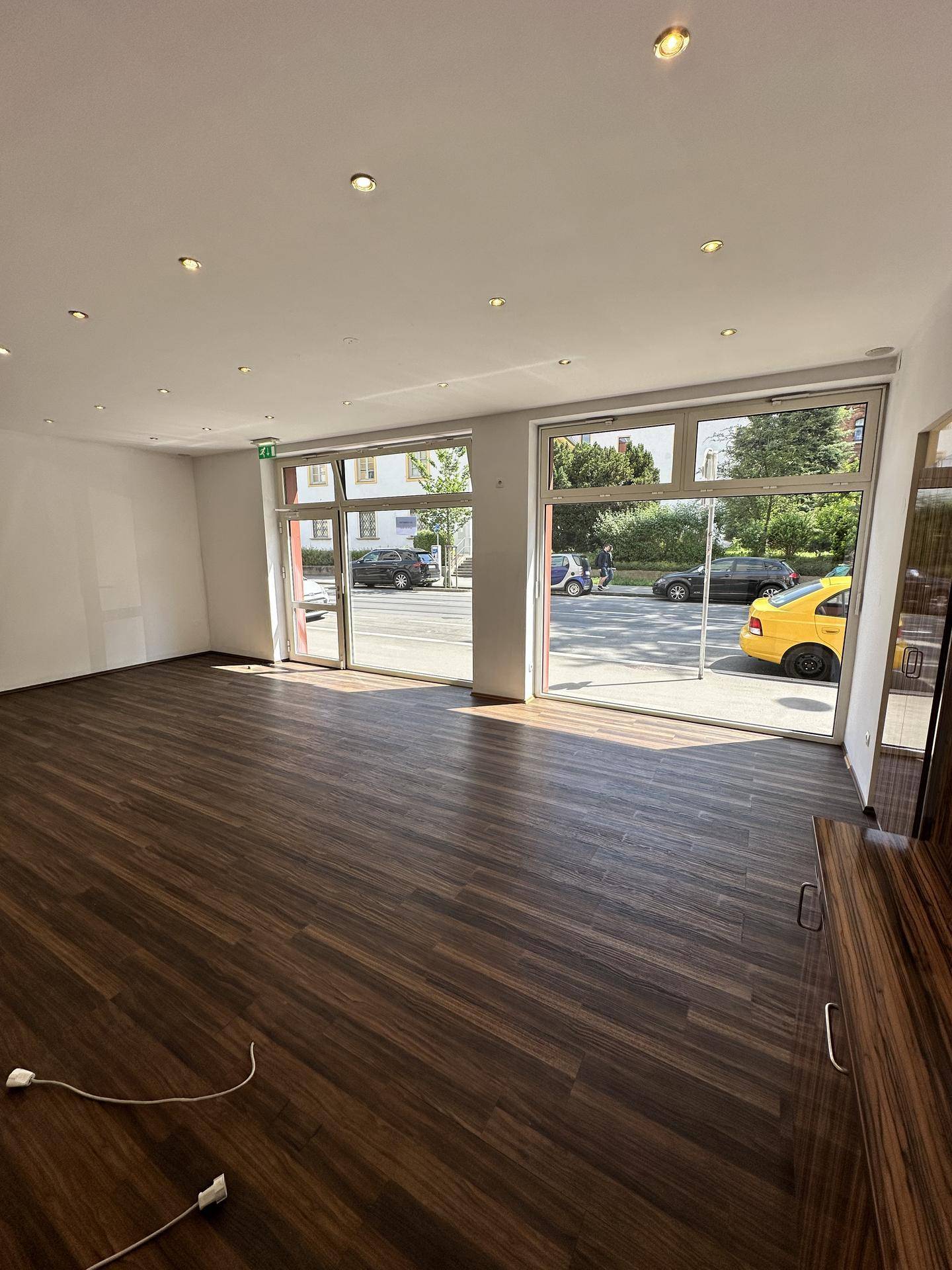 Geräumiger Geschäftsraum mit großen Fenstern, dunklem Holzboden und moderner Deckenbeleuchtung, leer und hell.