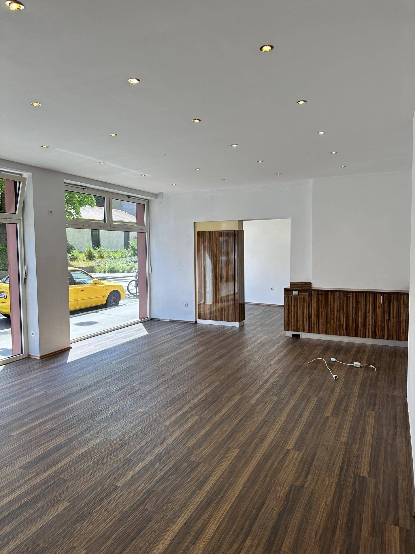 Offener Geschäftsraum mit großen Schaufenstern, dunklem Holzboden und moderner Deckenbeleuchtung.