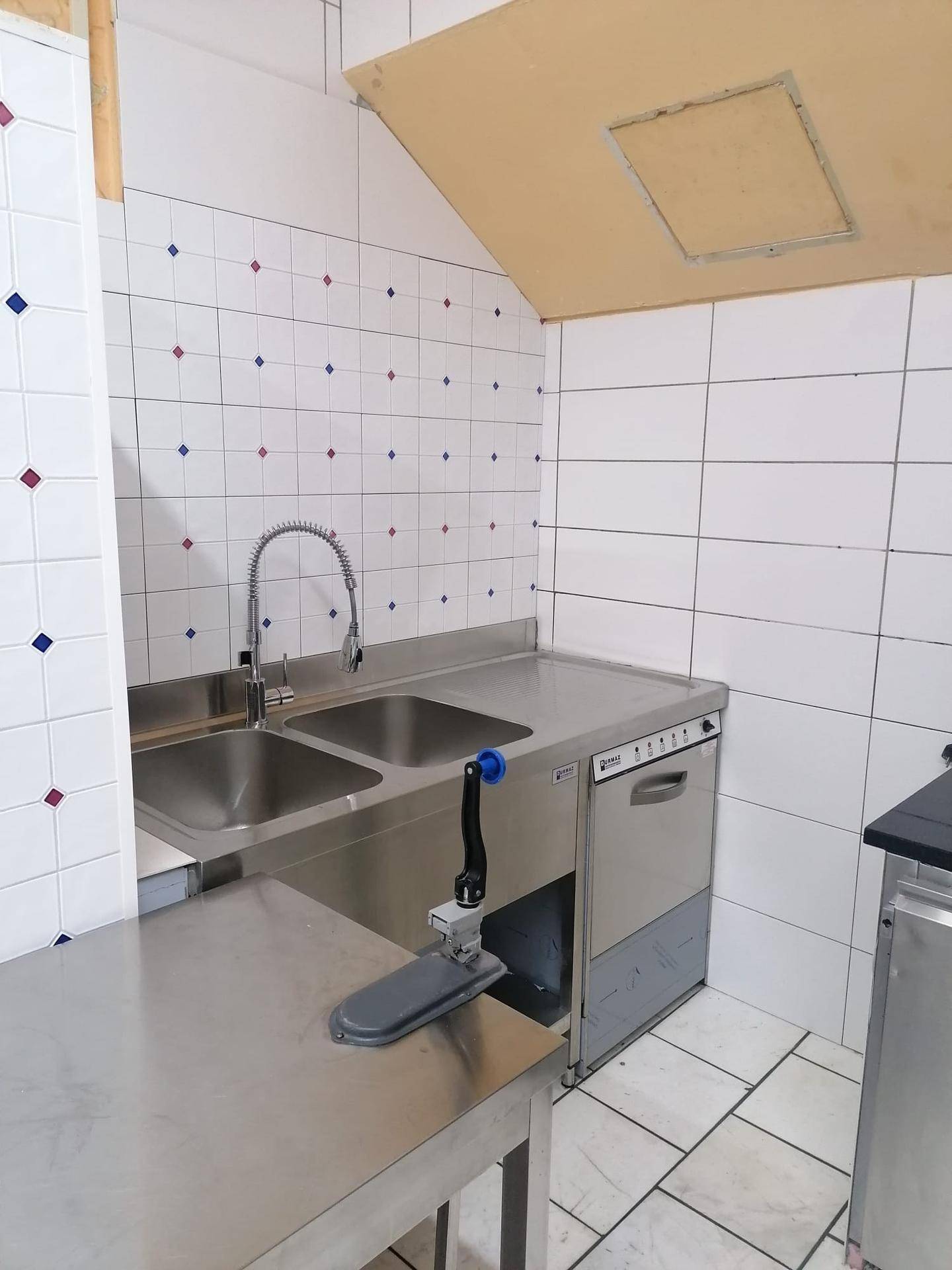 Spülbereich einer Gewerbeküche mit zwei Edelstahlspülbecken und einem Geschirrspüler.