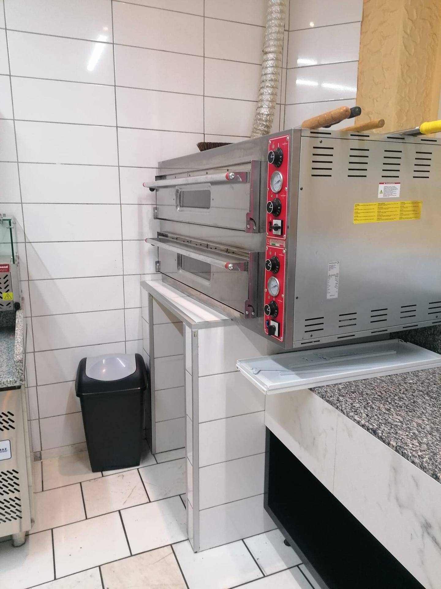 Professionelle Küche mit zwei großen Pizzaöfen und weißen Fliesen an den Wänden.