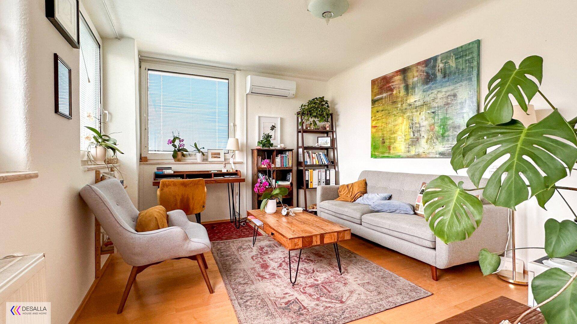 Gemütliches Wohnzimmer mit Sofa, Couchtisch und Bücherregal, hell durch großes Fenster.