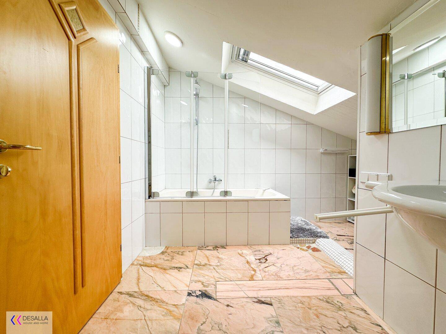 Helles Badezimmer mit Badewanne, Dusche und Dachfenster, ausgestattet mit Marmorboden.