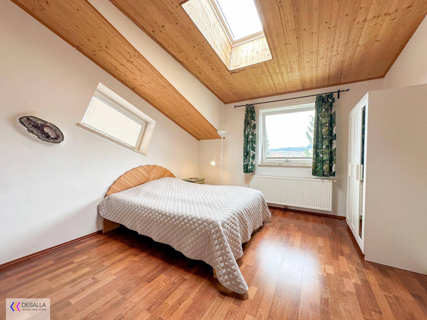 Gemütliches Schlafzimmer im Dachgeschoss mit Holzbalkendecke, Holzboden und Ausblick ins Grüne.