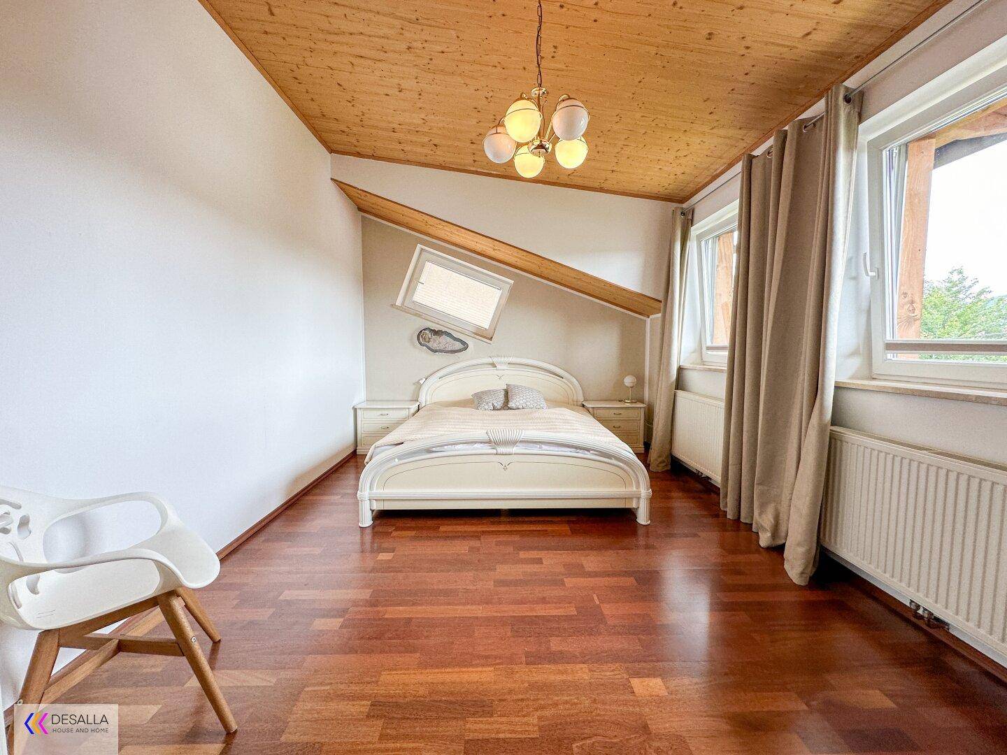 Helles Schlafzimmer im Dachgeschoss mit Holzbalkendecke, Holzboden und großem Fenster.