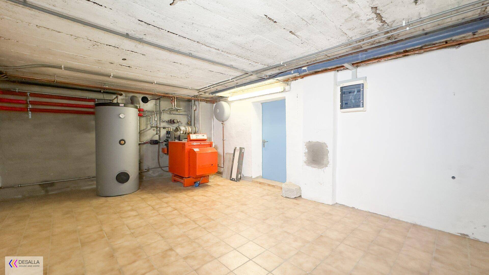 Heizungsraum im Keller mit Heizkessel, Warmwasserspeicher und gefliestem Boden.