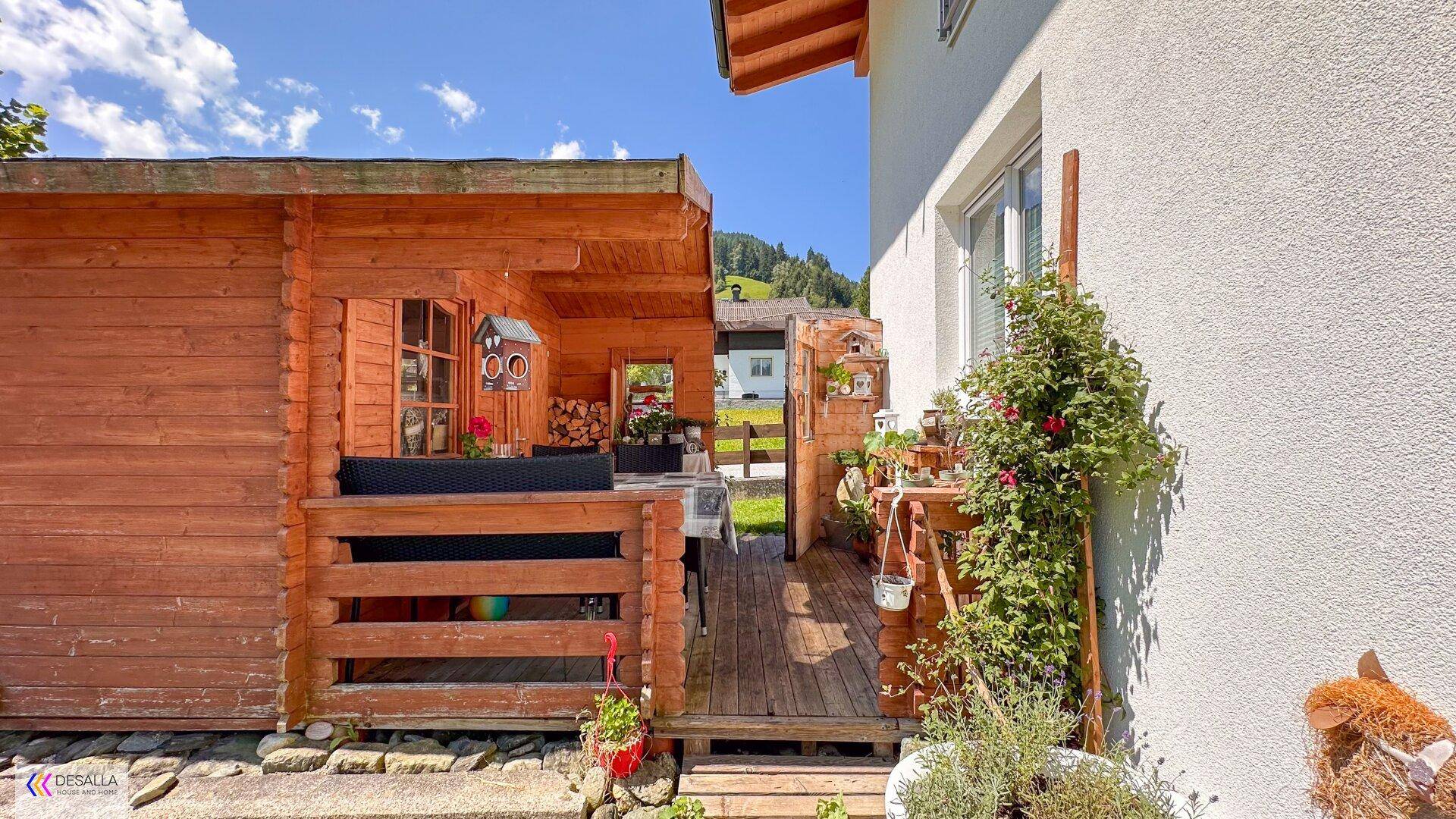 Rustikales Gartenhaus aus Holz mit überdachtem Sitzbereich und Dekoration.