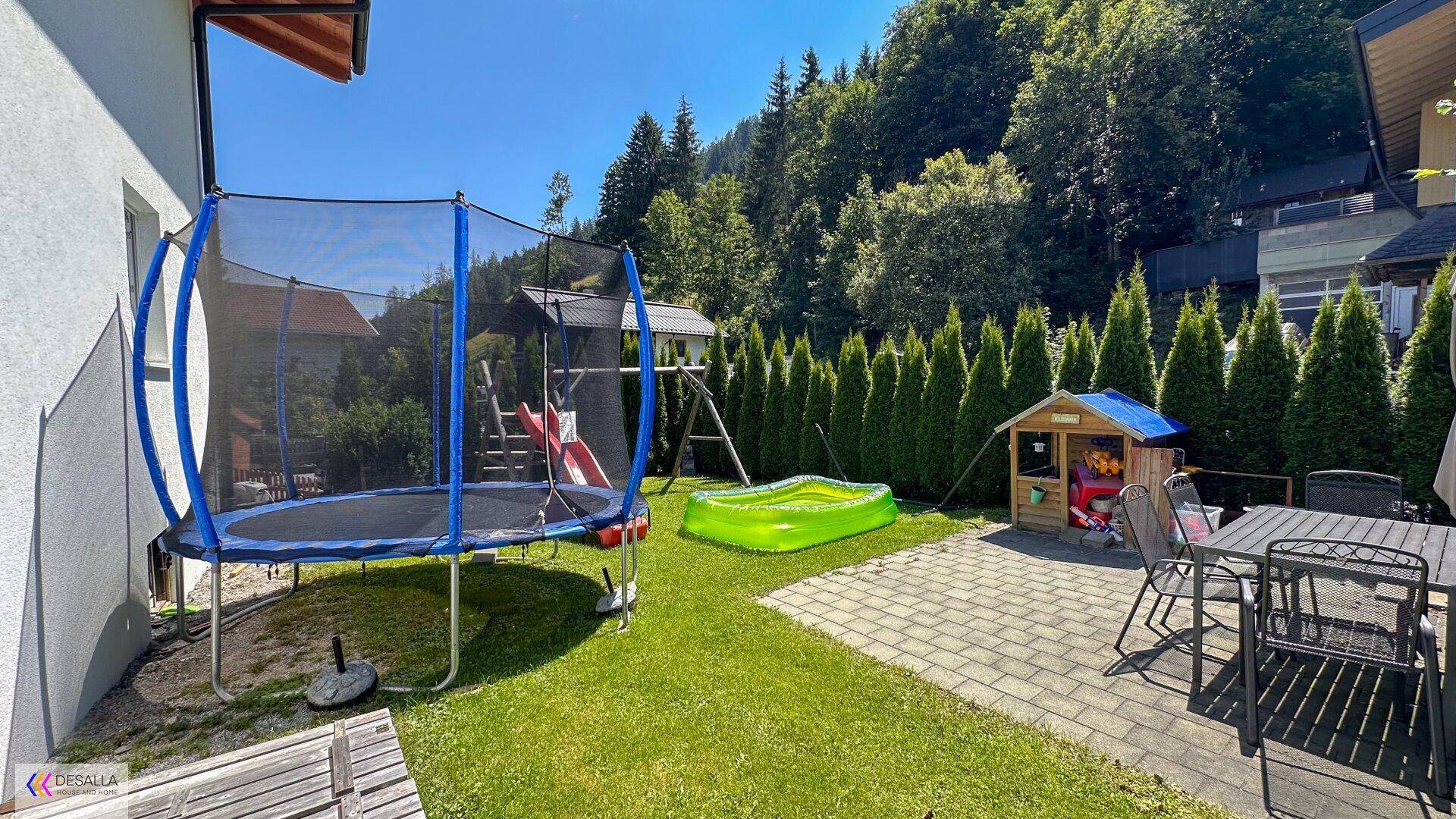 Gepflegter Gartenbereich mit Trampolin, Spielplatz, Terrasse und Hecken.
