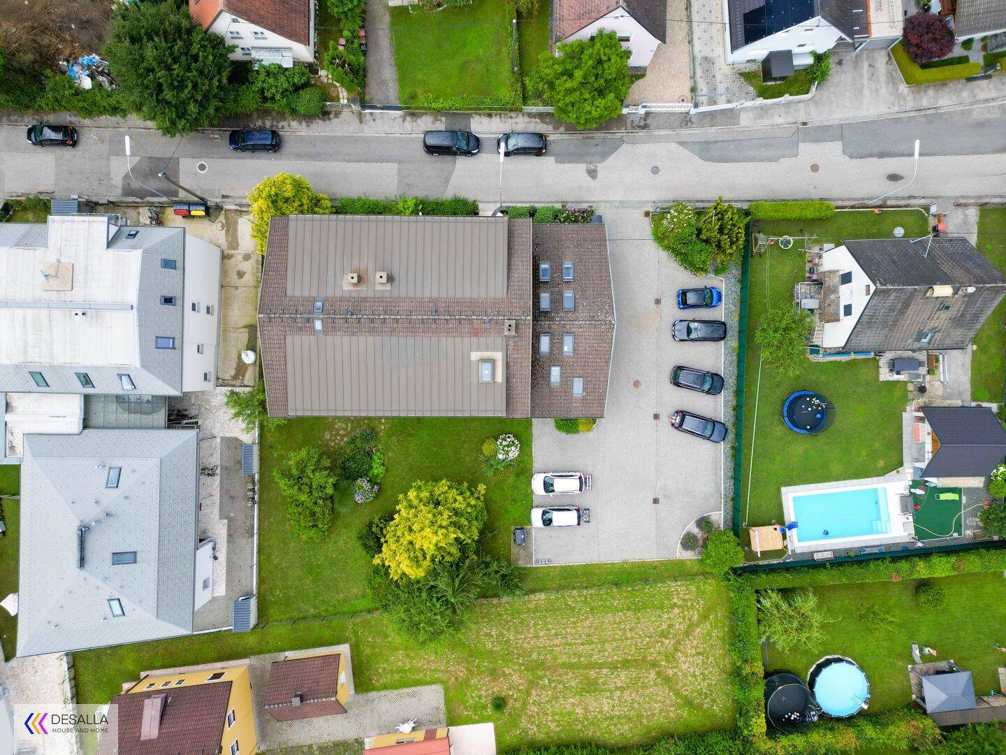 Vogelperspektive des Anwesens mit Gebäude, Parkplätzen und umliegenden Häusern in grüner Umgebung.