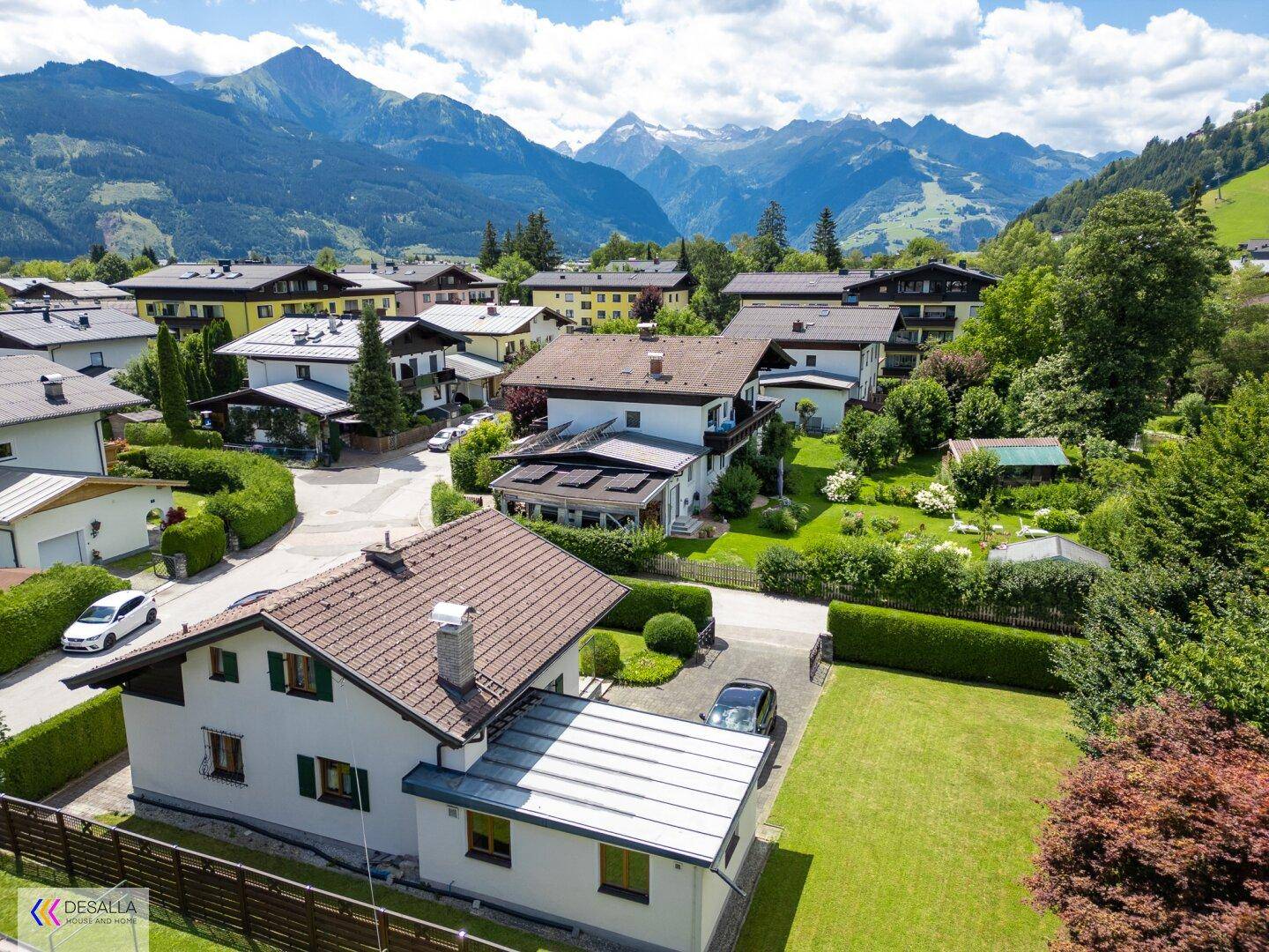 Panoramablick auf das Haus und die umliegende Wohnsiedlung vor einer beeindruckenden Berglandschaft.