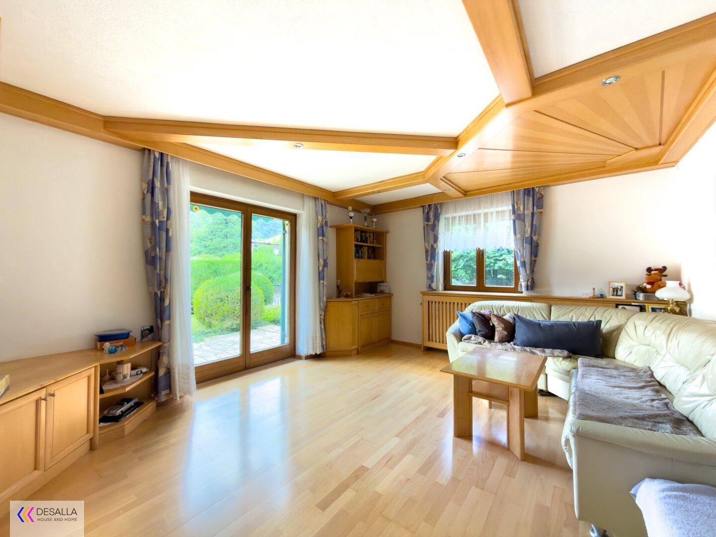 Gemütliches Wohnzimmer mit Holzbalkendecke, hellem Parkettboden und Zugang zum Garten.