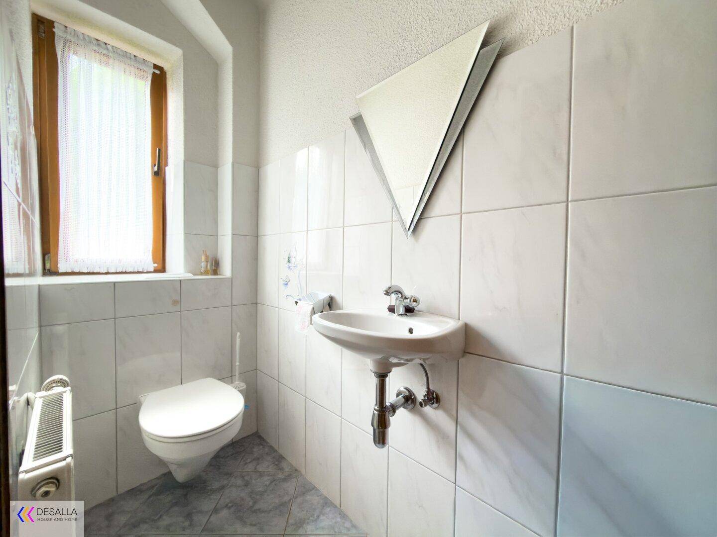 Helles Gäste-WC mit weißen Fliesen, kleinem Waschbecken und einem Fenster.