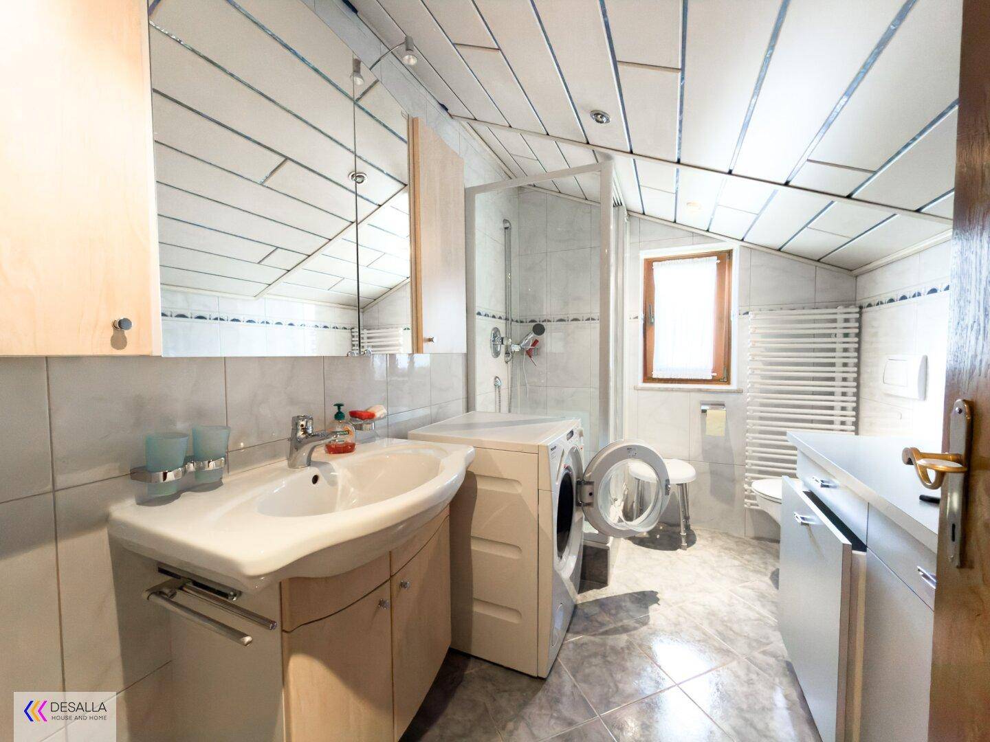 Badezimmer mit Dusche, Waschbecken, Waschmaschine und einer Dachschräge.