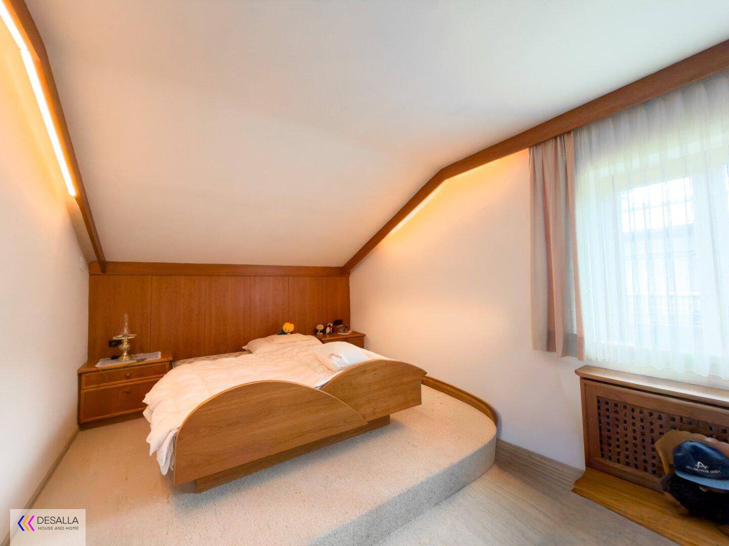 Schlafzimmer mit Bett auf Podest, Holzvertäfelung und einer gemütlichen Dachschräge.