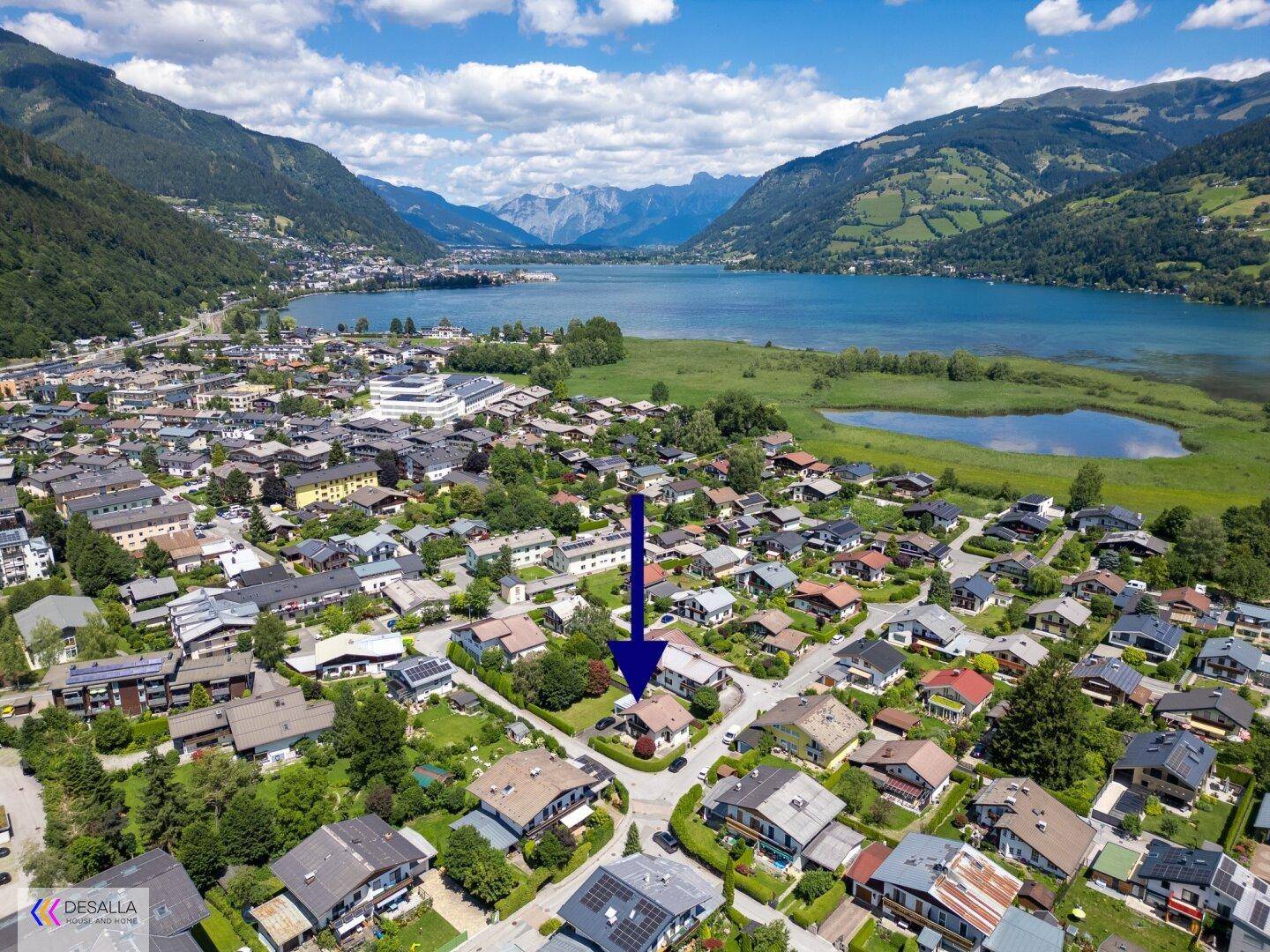 Luftaufnahme der Wohngegend mit See und majestätischer Bergkulisse, das Haus ist markiert.