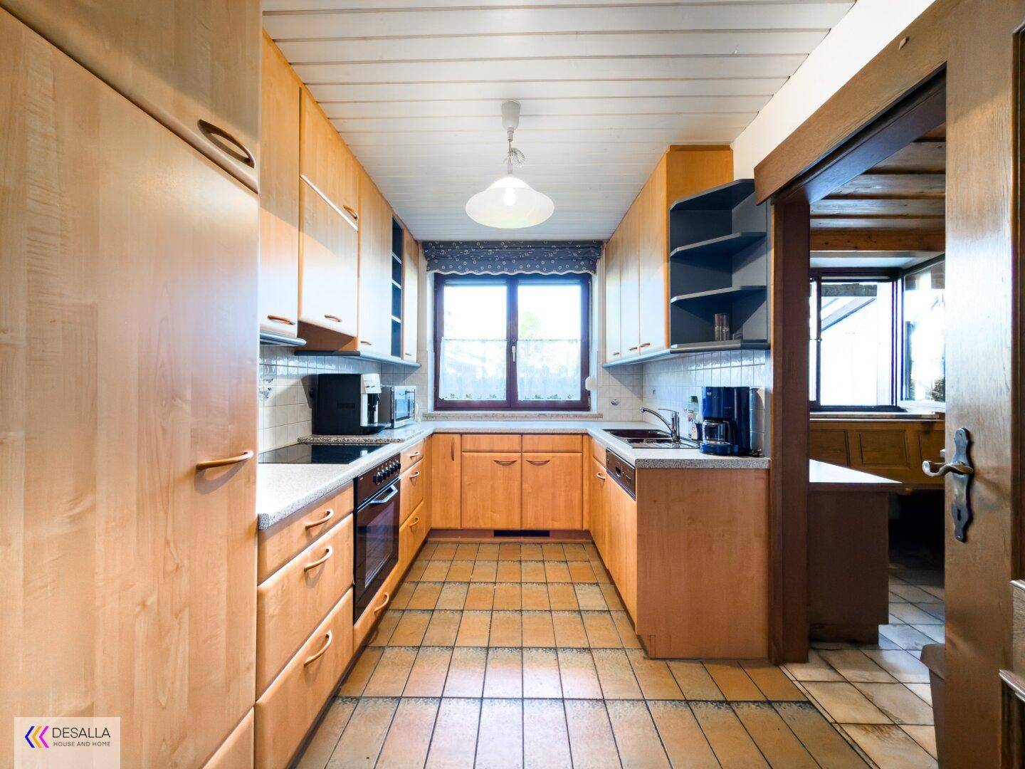 Funktionale Küche mit Holzschränken, Fliesenboden und Fenster über der Spüle.