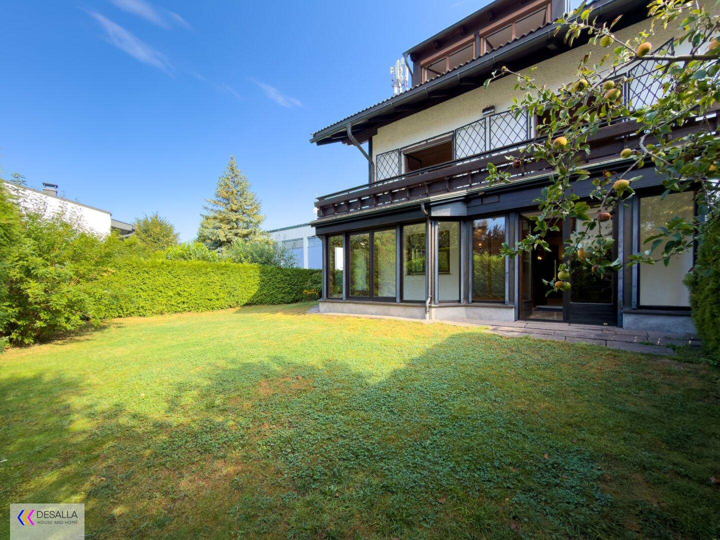 Gepflegter Garten mit Rasenfläche, Hecke und Blick auf das Haus mit Wintergarten.
