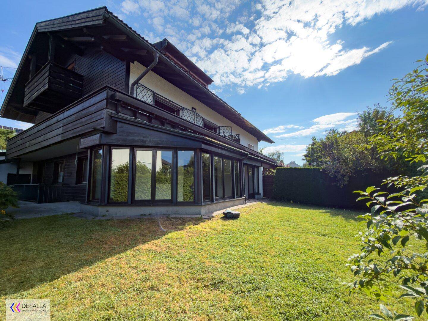 Sonnige Rasenfläche im Garten neben dem Haus mit großen Fenstern und Balkonen.