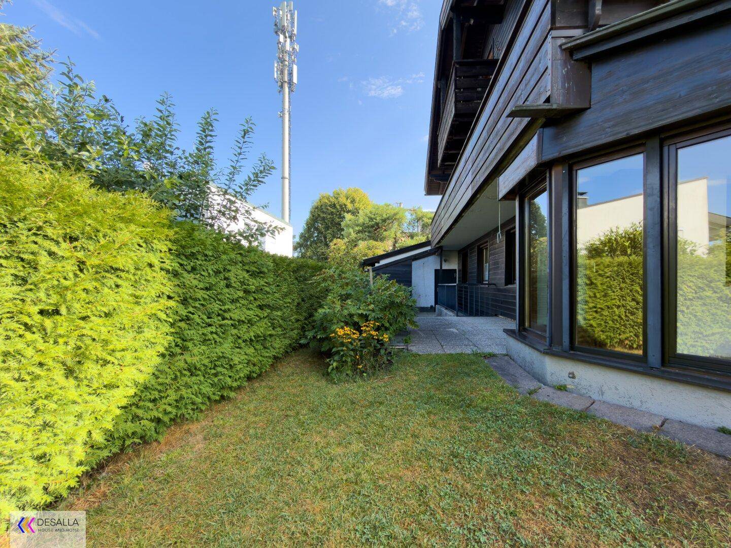 Seitlicher Gartenbereich mit Rasen, Hecke und einem kleinen gepflasterten Weg.