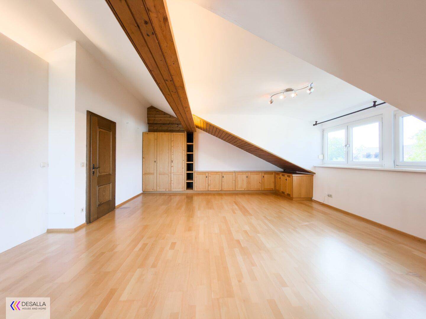 Geräumiges Dachgeschosszimmer mit Holzbalken, Parkettboden und Einbauschränken.