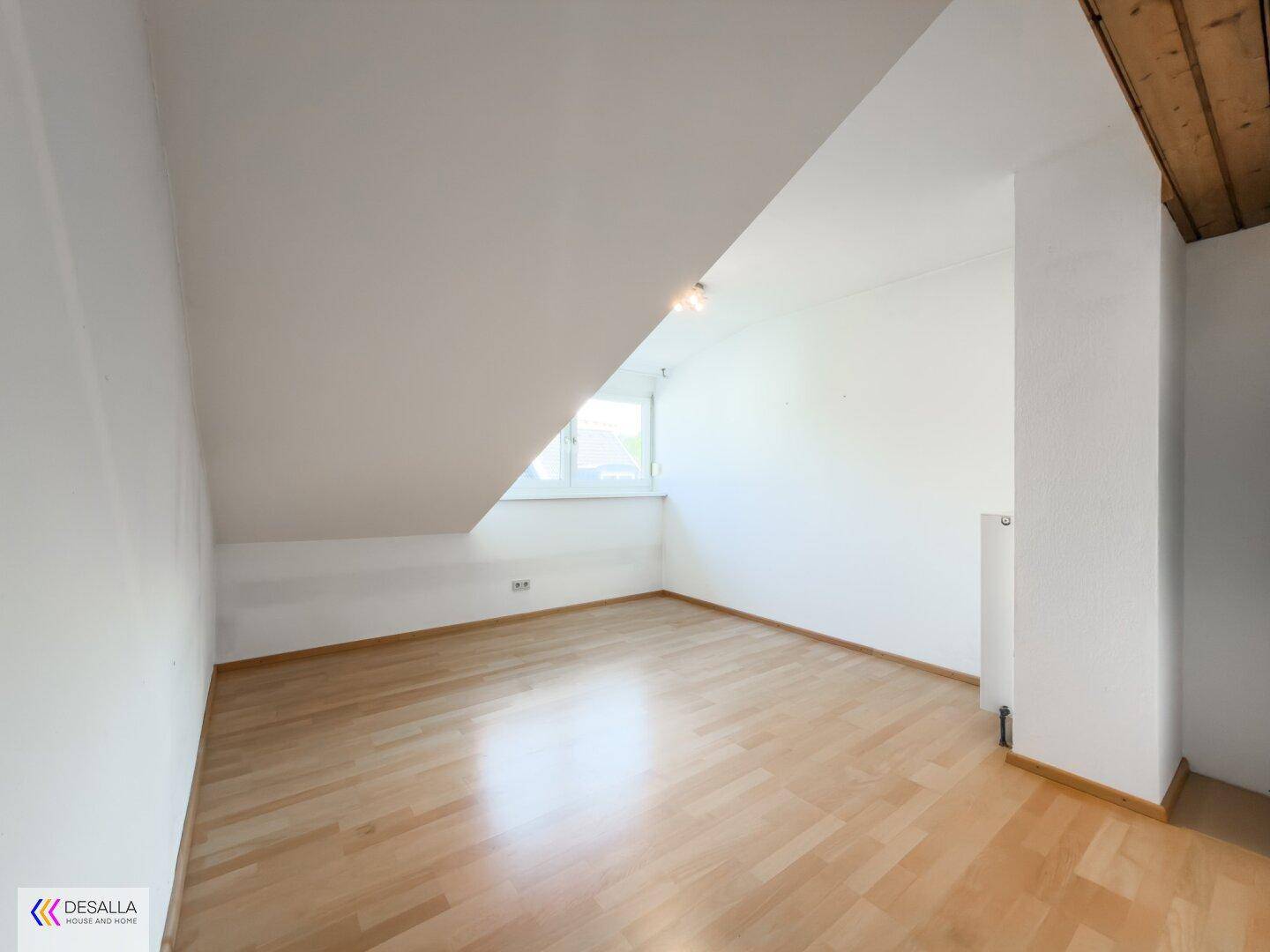 Helles Zimmer im Dachgeschoss mit Parkettboden und schrägen Wänden.