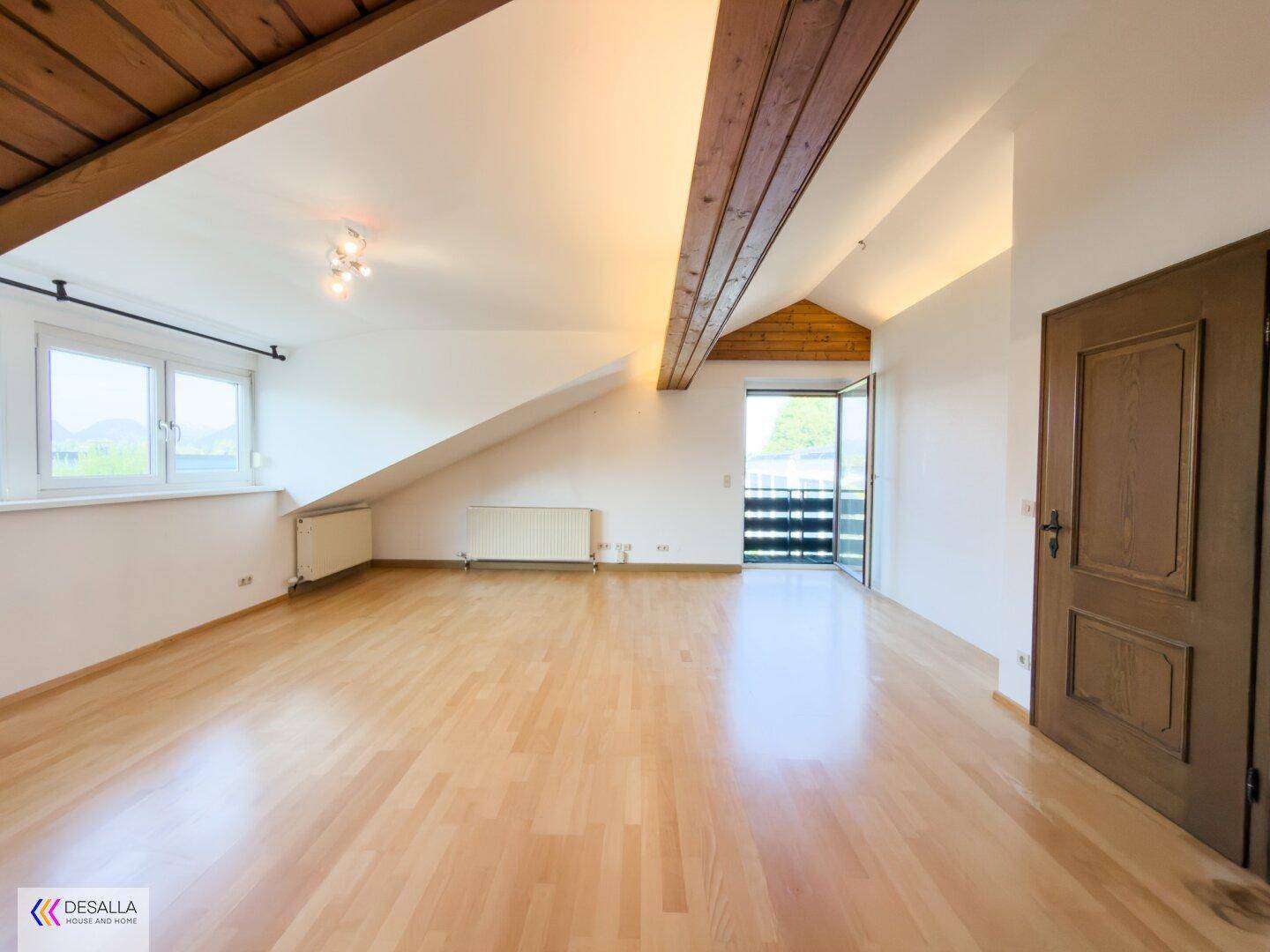 Helles Dachgeschosszimmer mit Holzbalken, Parkettboden und Balkonzugang.