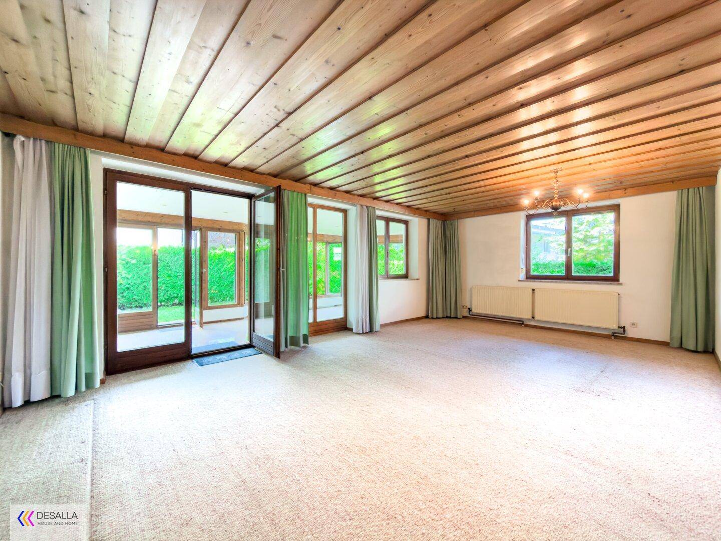 Geräumiges Wohnzimmer mit Teppichboden, Holzdecke und Zugang zum Wintergarten.