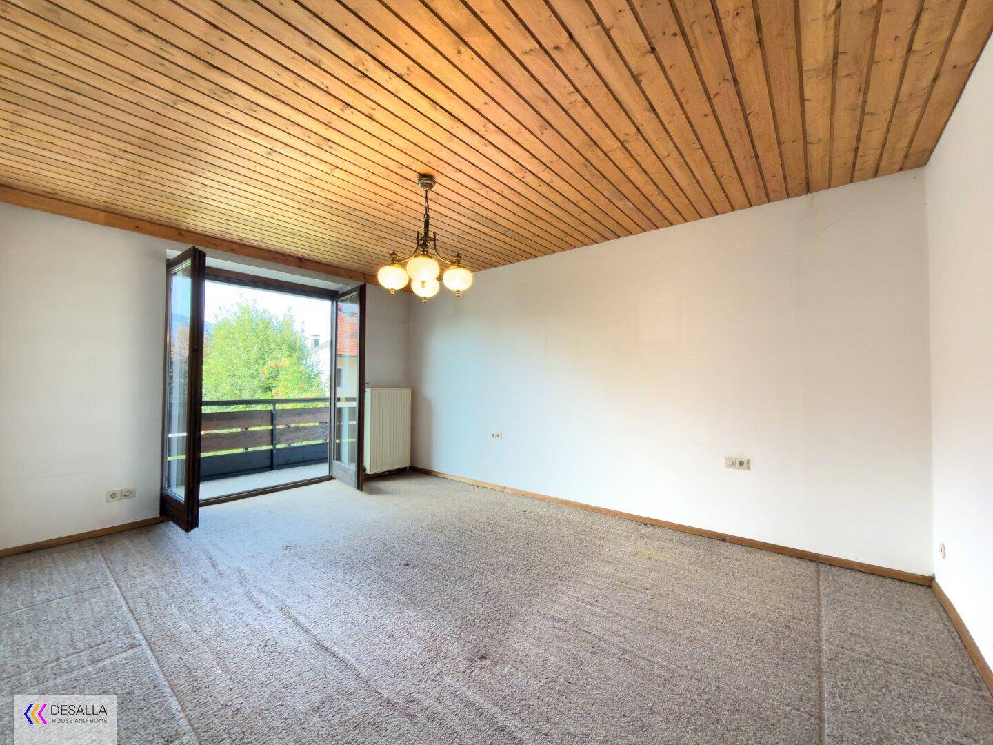 Helles Zimmer mit Teppichboden, Holzdecke und Zugang zu einem Balkon.