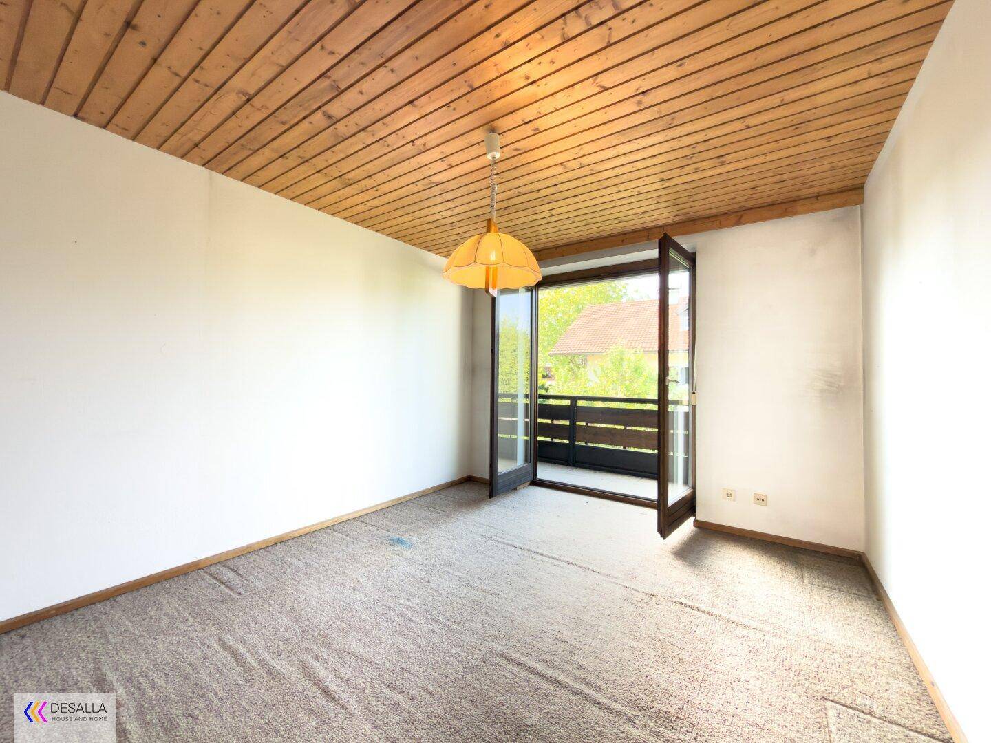 Schlafzimmer mit Teppichboden, Holzdecke und Zugang zu einem Balkon.