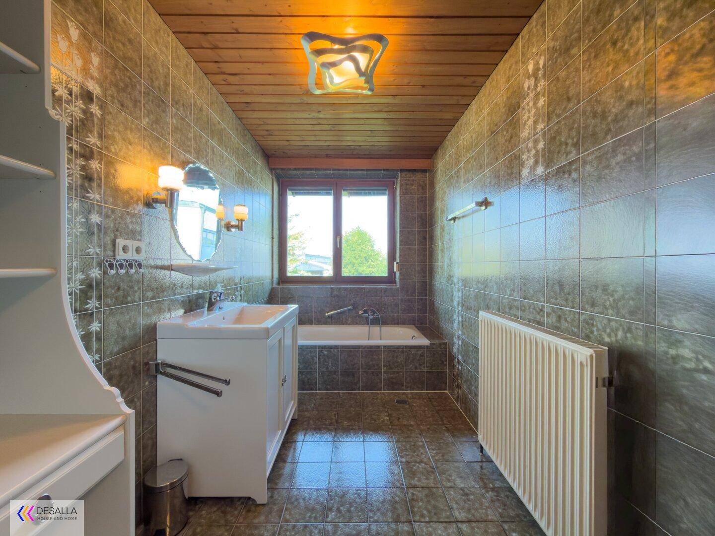 Badezimmer mit Badewanne, Waschbecken, Fliesenwänden und Holzdecke.