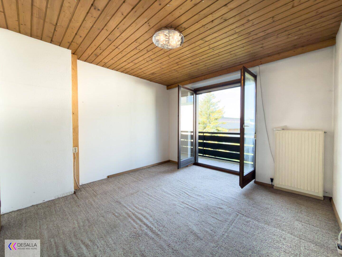 Helles Schlafzimmer mit Teppichboden, Holzdecke und Balkonzugang.