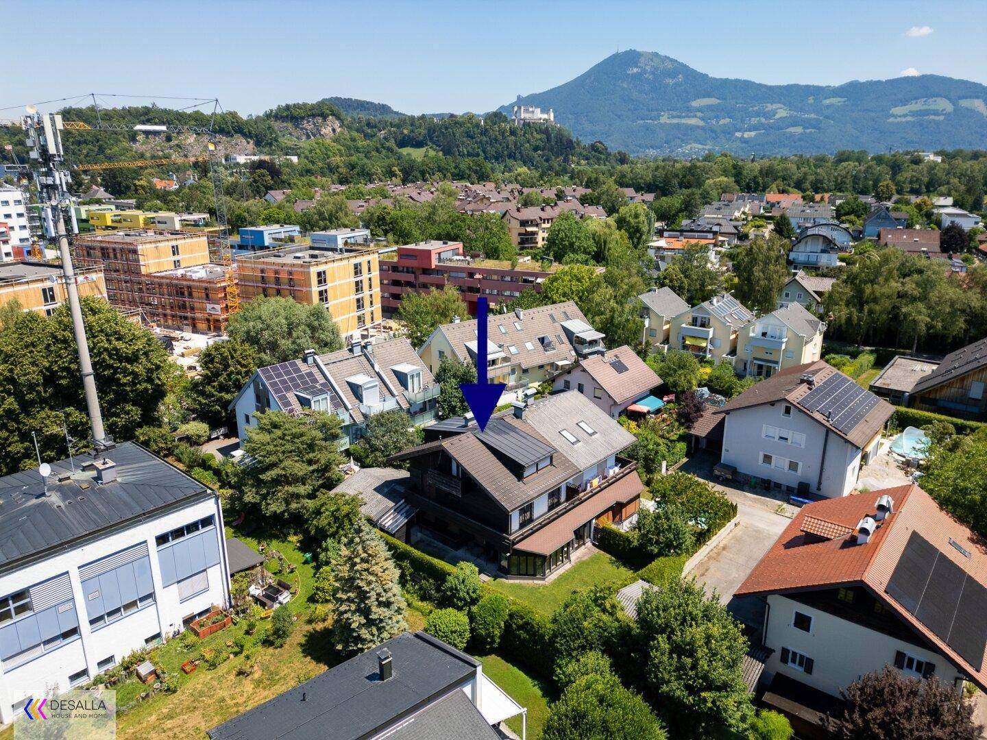 Luftaufnahme des Hauses in einer Wohngegend mit umliegenden Gebäuden und Bergen im Hintergrund.