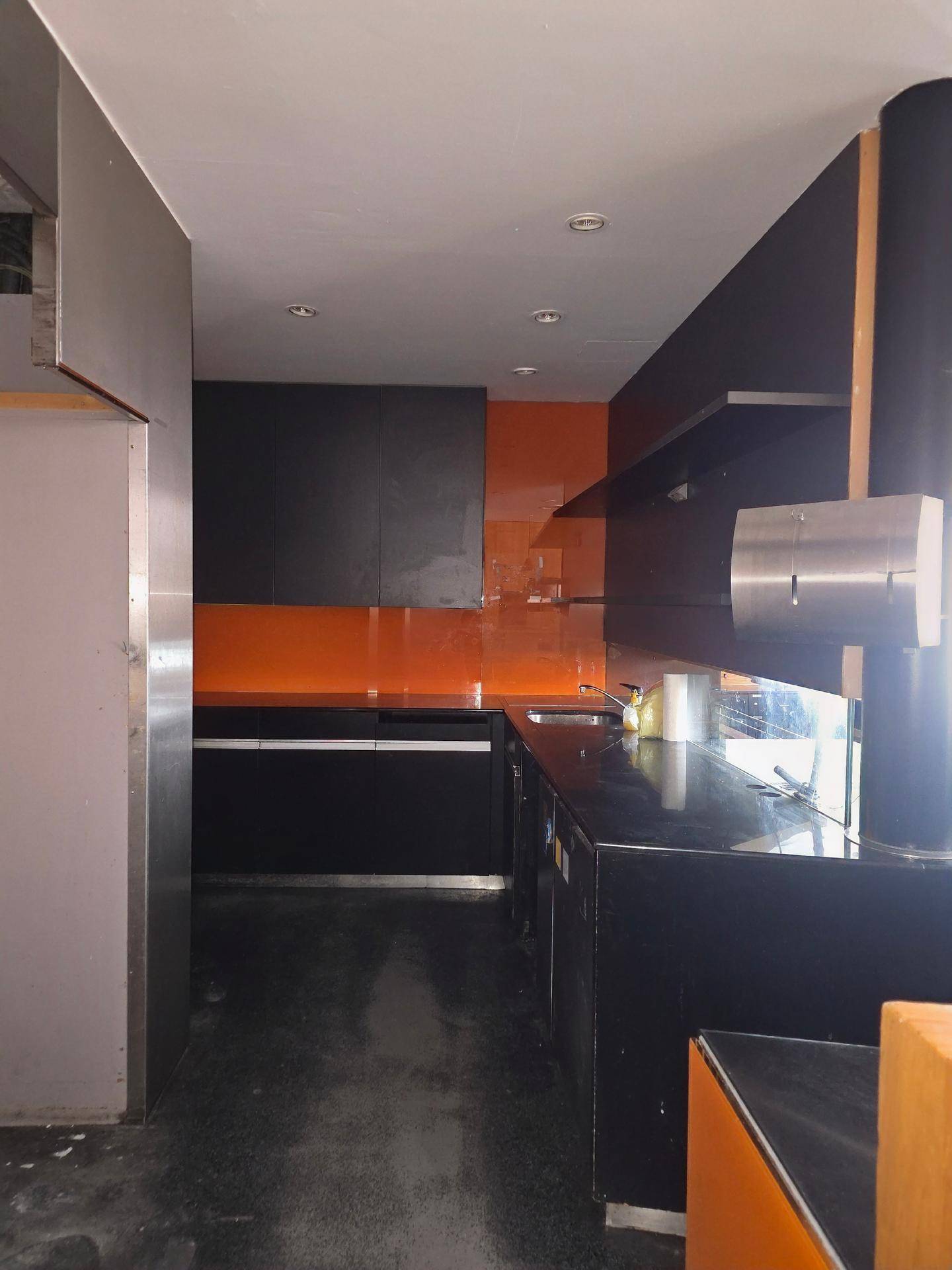 Moderne Küche mit schwarzen Schränken, dunklen Arbeitsplatten und leuchtend orangefarbenen Wandpaneelen.