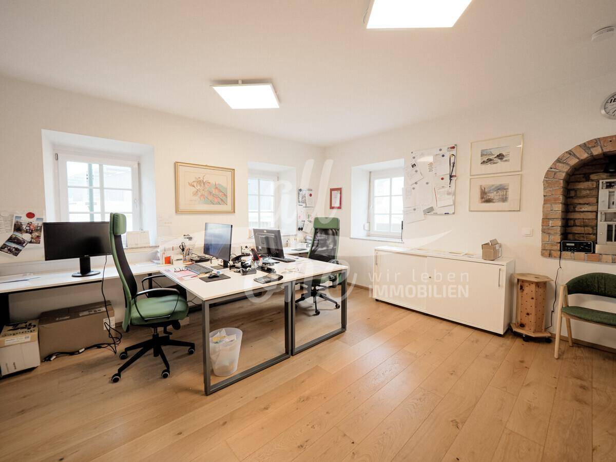 Geräumiges Büro mit mehreren Arbeitsplätzen, Holzboden und einem dekorativen Ziegelbogen.