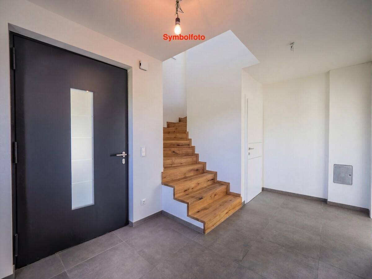 Heller Eingangsbereich mit modernen Fliesen und einer eleganten Holztreppe ins Obergeschoss.