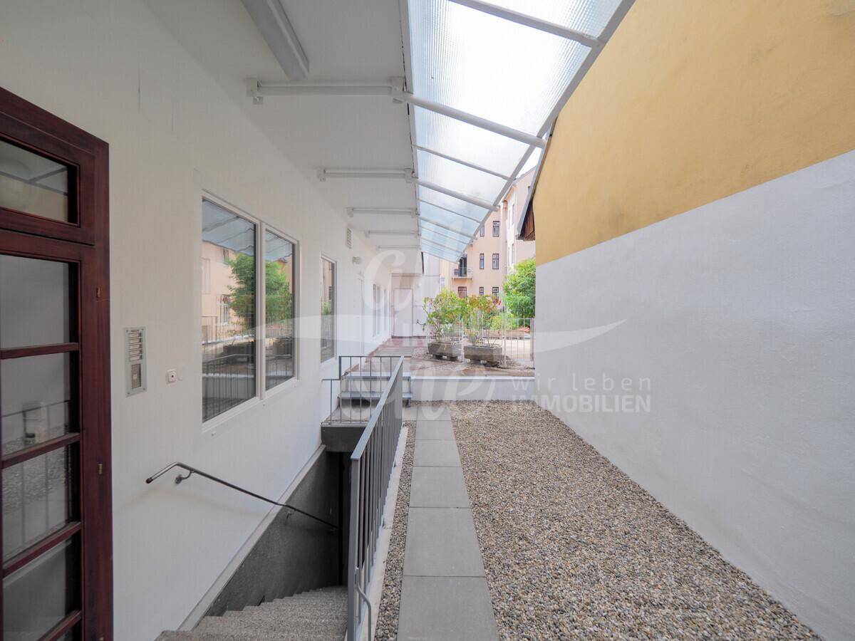Überdachter Außenbereich mit Kiesweg und Zugang zu den Wohneinheiten und dem Keller.