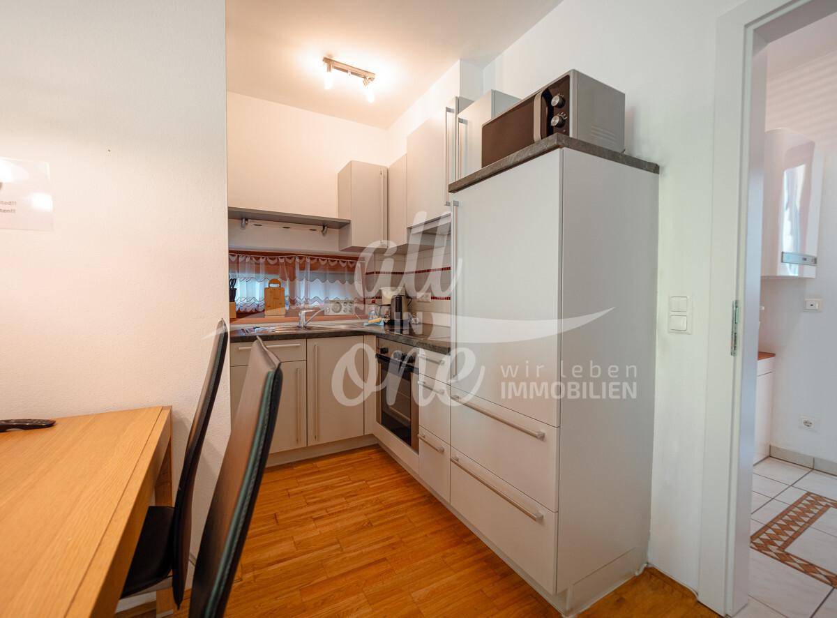 Funktionale Küche mit hellen Schränken, integriertem Backofen und Mikrowelle, sowie Holzboden.