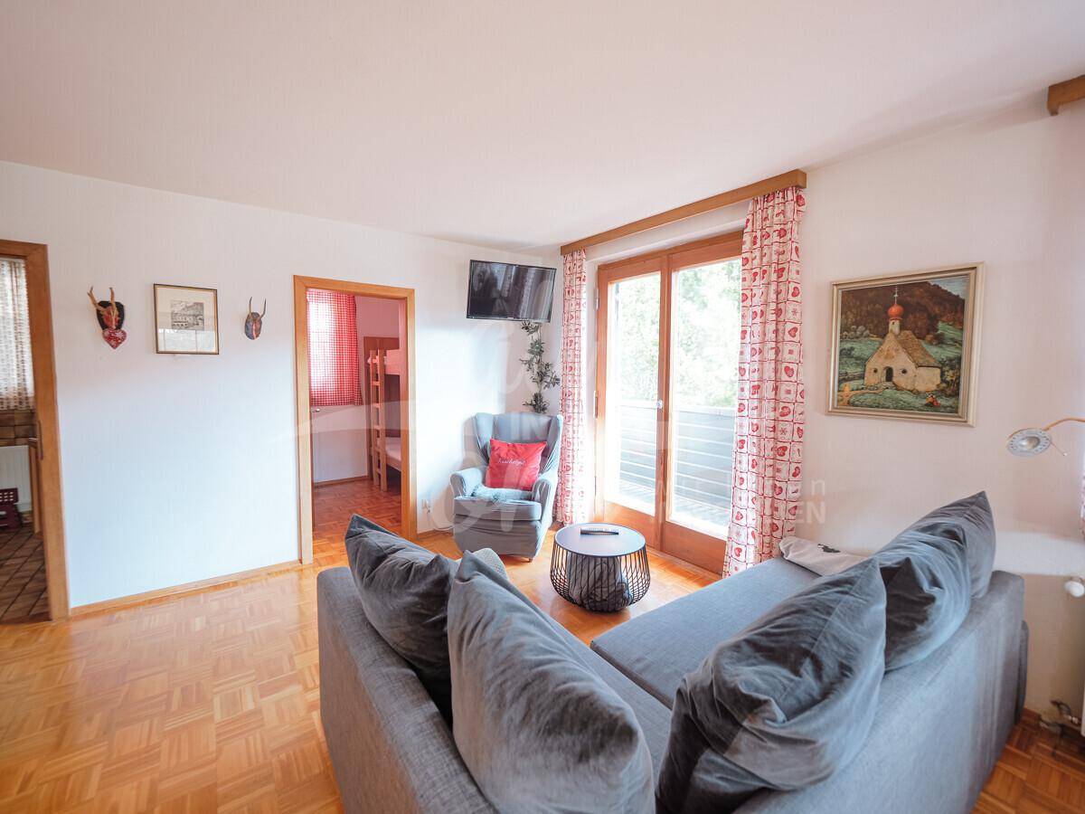 Heller Wohnbereich mit bequemer Couch, Parkettboden und Zugang zum Balkon.