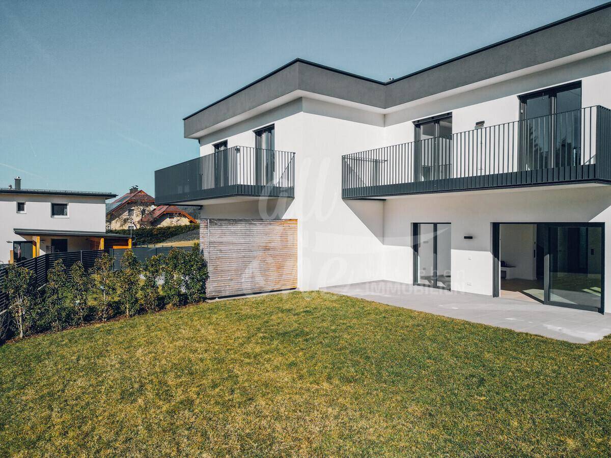 Ansicht eines modernen Hauses mit gepflegtem Rasen, Terrasse und Balkonen im Obergeschoss.