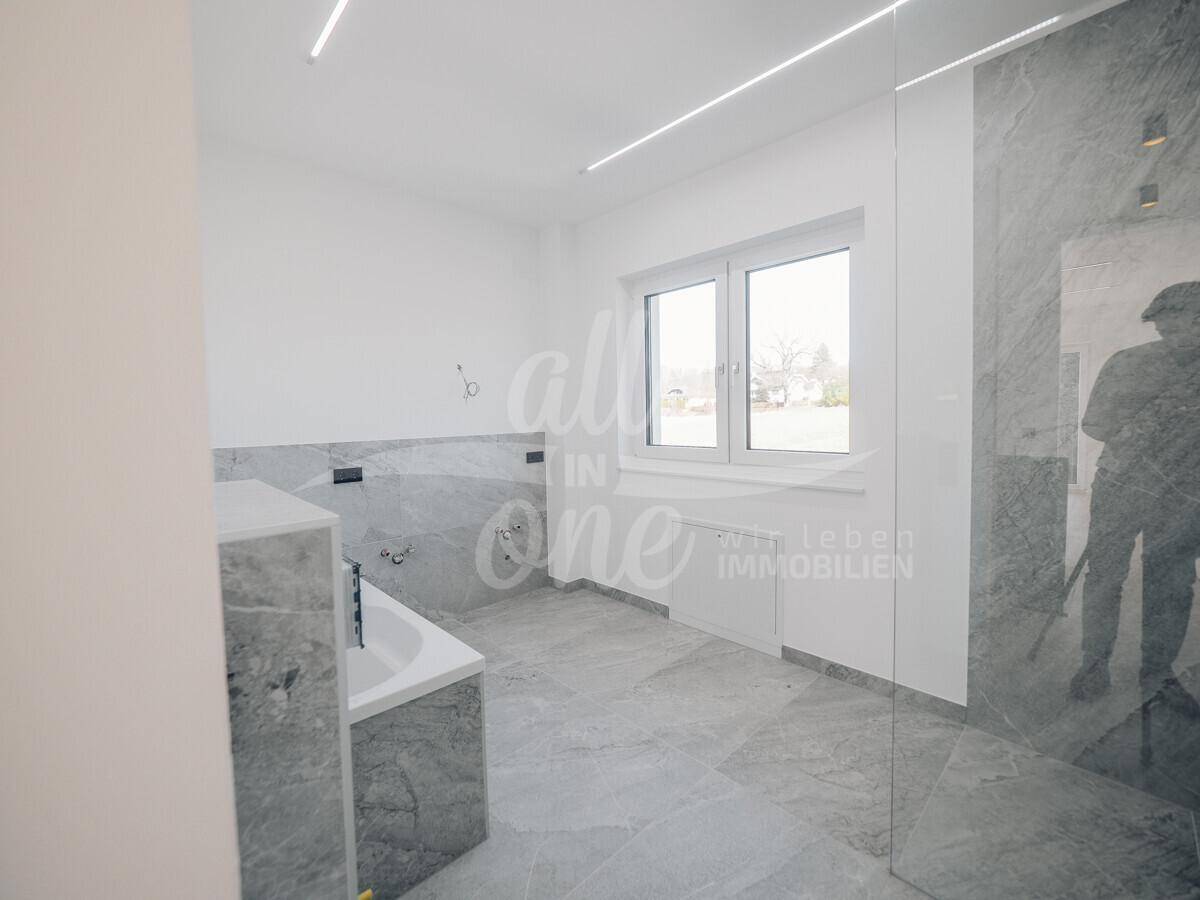 Modernes Badezimmer mit großen grauen Fliesen, Badewanne und begehbarer Dusche.