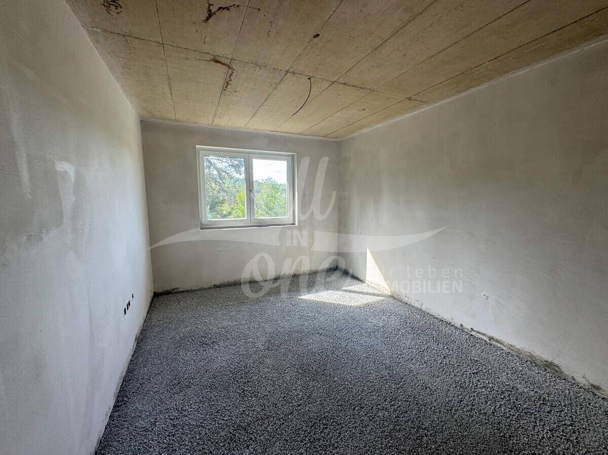 Unfertiges Schlafzimmer im Rohbau mit einem Fenster und Blick auf die Natur.
