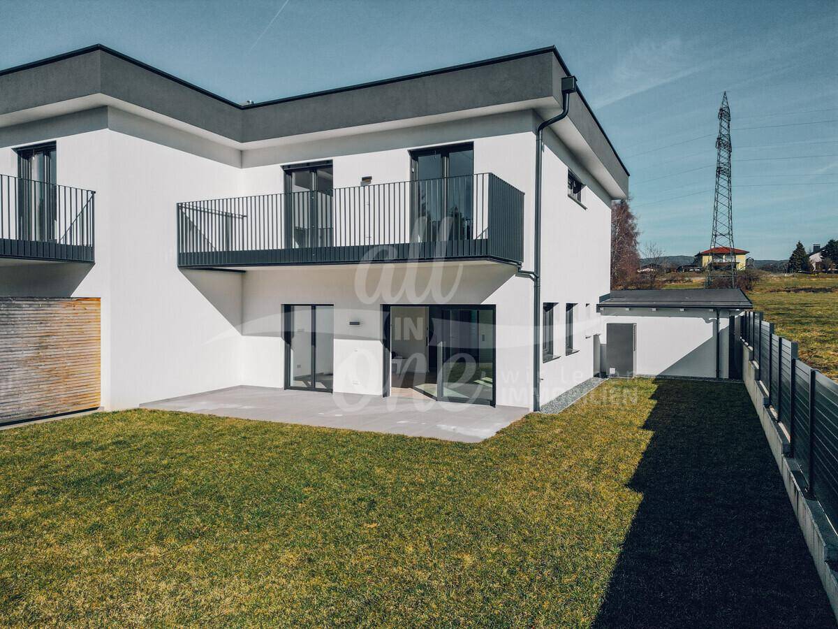 Rückseite eines modernen Hauses mit gepflegtem Rasen, Terrasse und Balkonen im Obergeschoss.