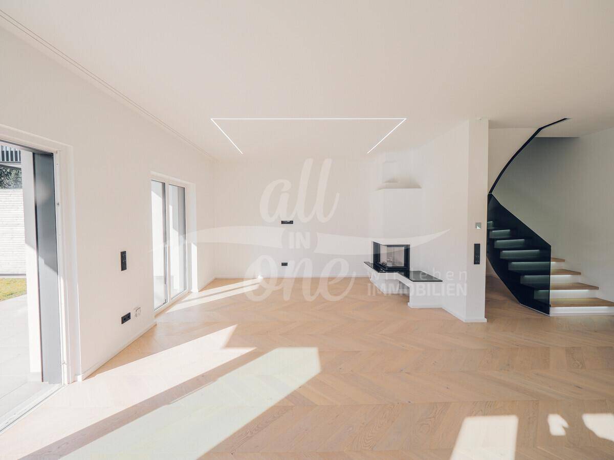 Geräumiges Wohnzimmer mit modernem Kamin, Fischgrätparkett und offener Treppe.