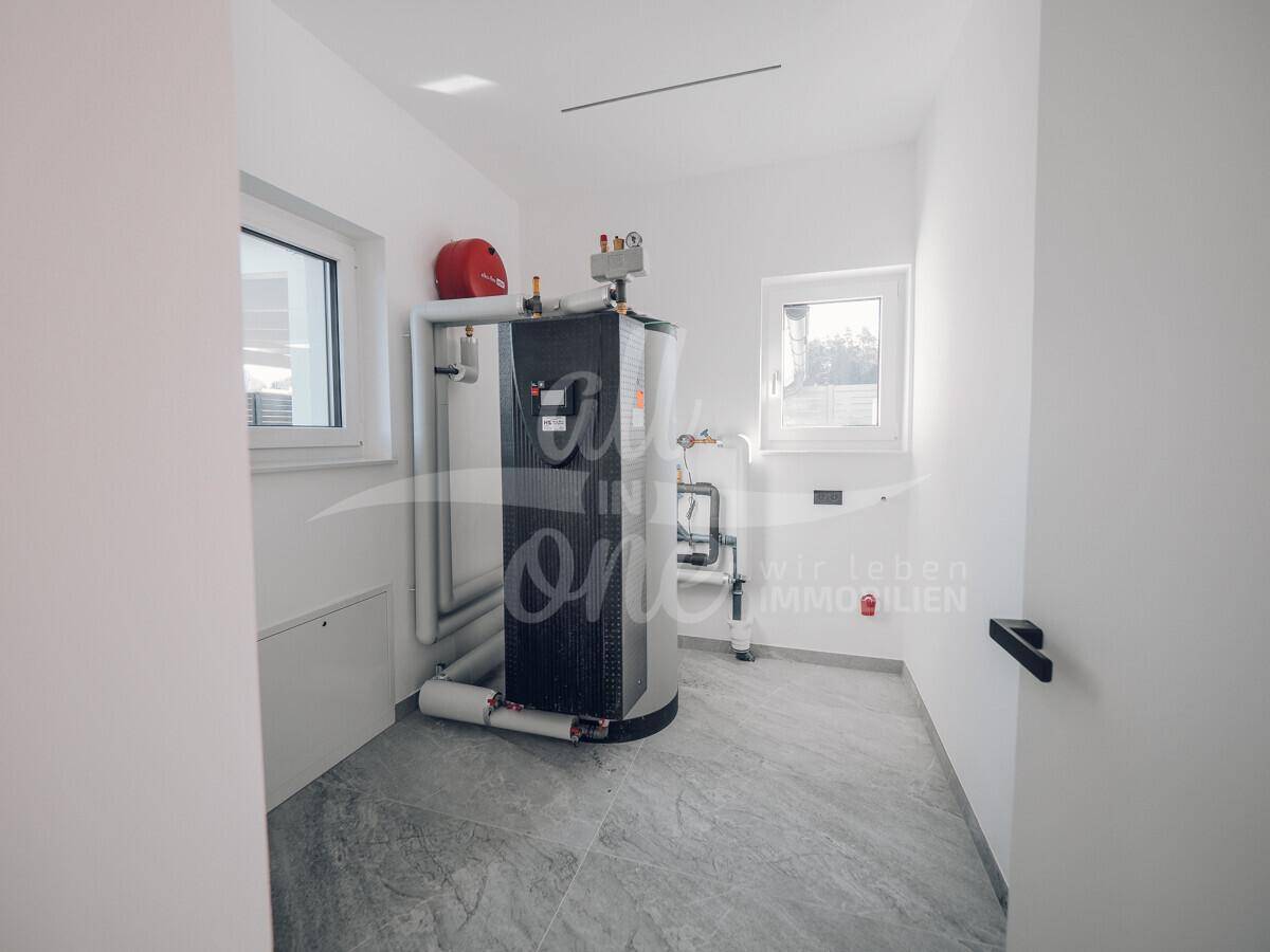 Funktionaler Hauswirtschaftsraum mit Warmwasserspeicher, Fliesenboden und zwei Fenstern.