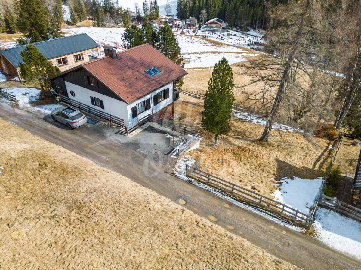 Das Haus von oben mit Zufahrtsweg und angrenzenden Grundstücken in der Berglandschaft.