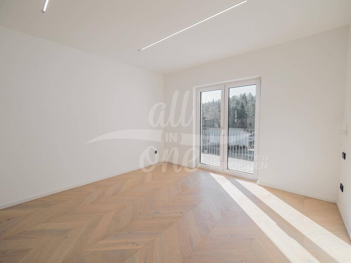Lichtdurchfluteter Wohnraum mit elegantem Fischgrätparkett und Zugang zu einem kleinen Balkon.