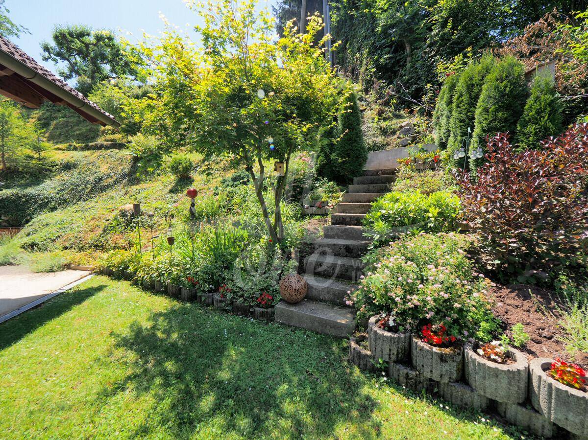 Gepflegter Garten mit Rasenfläche, Blumenbeeten und Steintreppe am Hang.