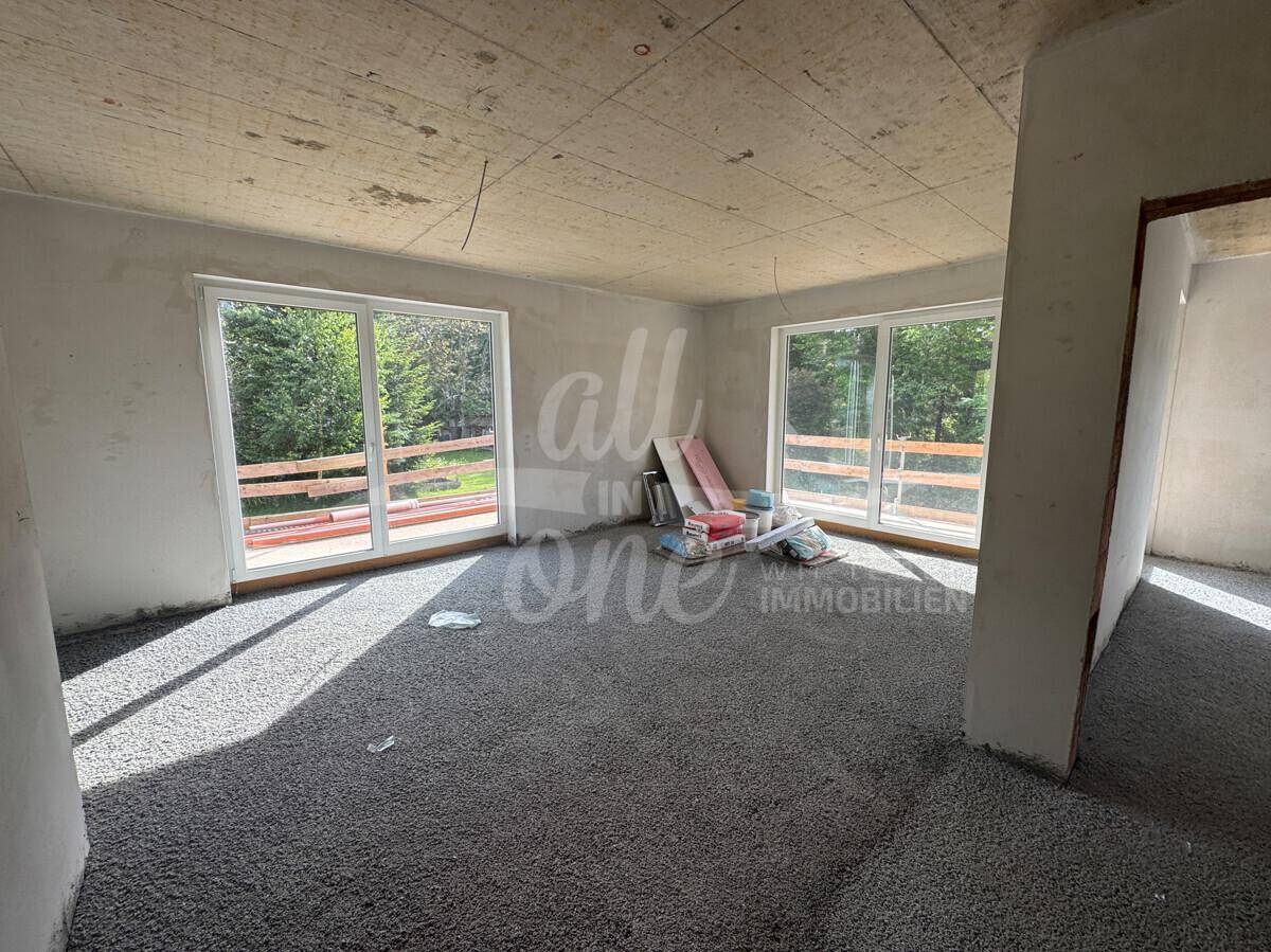 Geräumiger Rohbau-Wohnraum mit großen Fenstern und Blick ins Grüne.