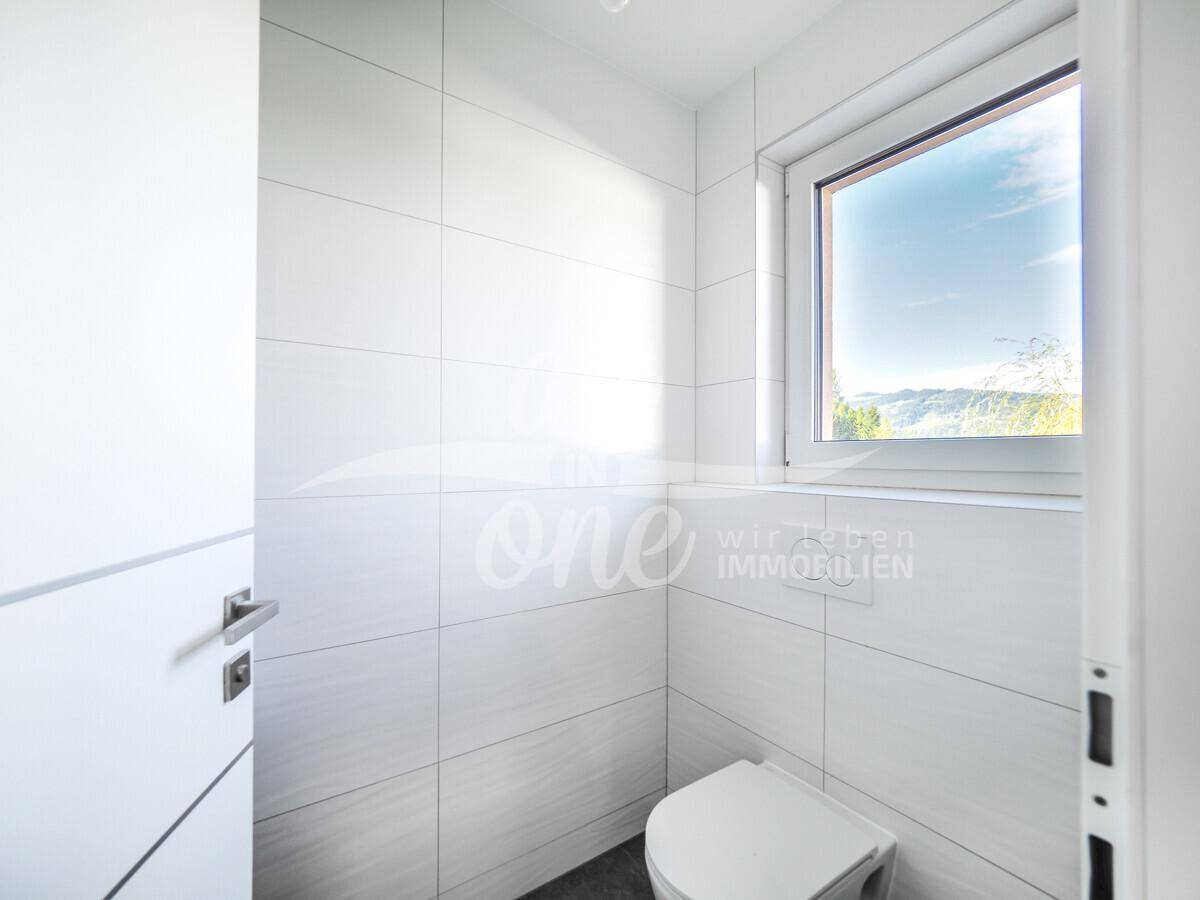 Modernes Gäste-WC mit weißen Fliesen, wandhängendem WC und Fenster für Tageslicht.